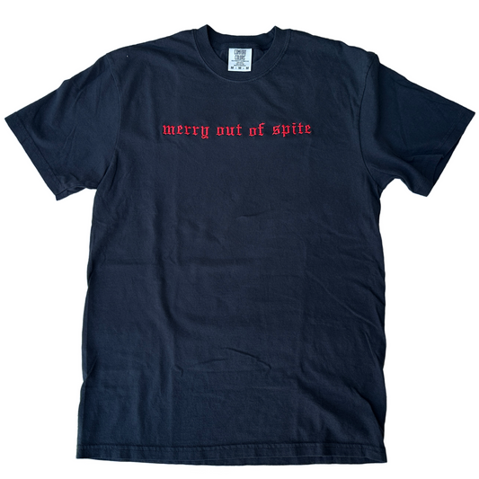 Black Comfort Colors short-sleeve T-shirt featuring red Old English gothic embroidery reading “merry out of spite” across the upper chest. Classic crewneck collar with a relaxed fit, displayed flat against a white background.