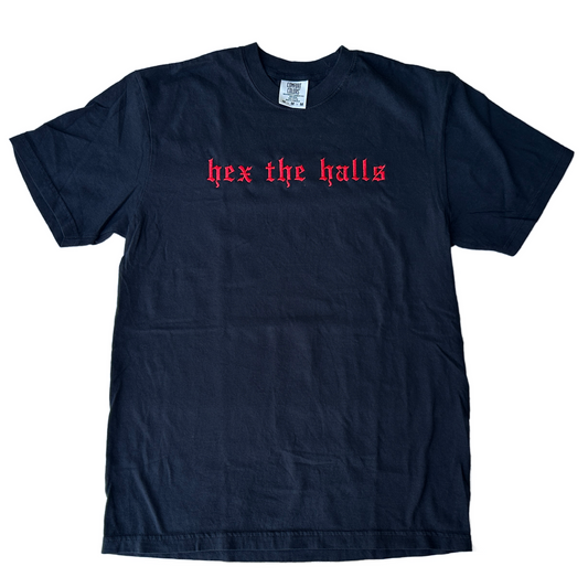 Black Comfort Colors short-sleeve T-shirt featuring red Old English gothic embroidery reading “hex the halls” across the upper chest. Classic crewneck collar with a relaxed fit, displayed flat against a white background.