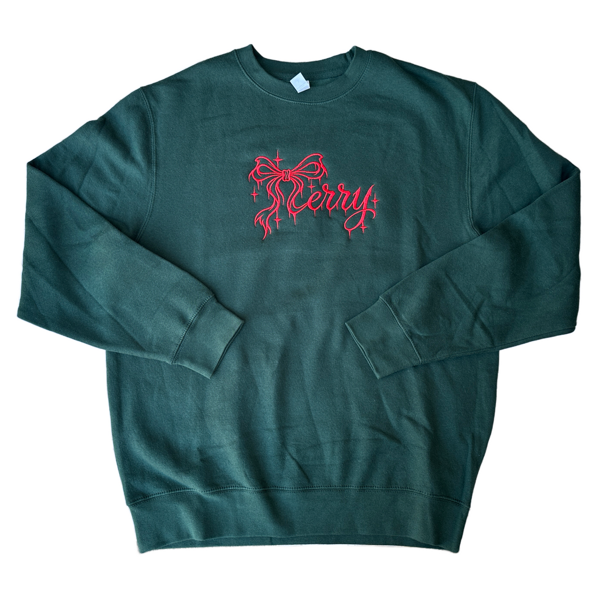 Dark forest green crewneck sweatshirt featuring red embroidered “Merry” lettering in elegant script, accented with a decorative bow and sparkling stars across the chest.