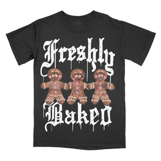 Black graphic tee with a design of three cartoon gingerbread figures and the text 'freshly baked' in a bold, dripping font.