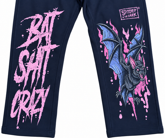 Black sweatpants featuring a distressed pink “Bat Shit Crazy” graphic on one leg and a blue and black bat with pink accents and Stitched in the Dark logo on the other leg.
