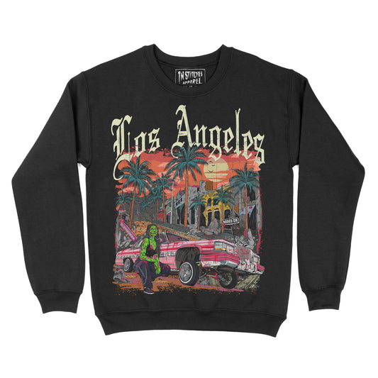 Black crewneck sweatshirt featuring the phrase ‘Los Angeles’ above a colorful illustration of palm trees, a lowrider car, and a sunset city scene. Zombie girl models by car