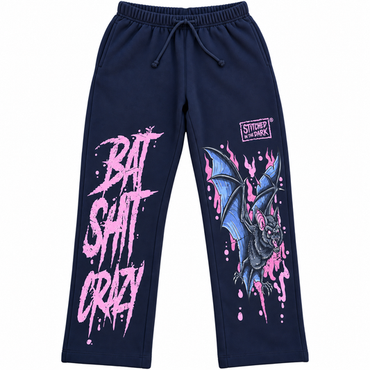 Black sweatpants featuring a distressed pink “Bat Shit Crazy” graphic on one leg and a blue and black bat with pink accents and Stitched in the Dark logo on the other leg.