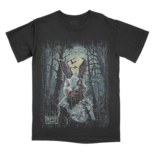 Black T-shirt featuring a creepy white rabbit with glowing red eyes and blood around its mouth standing in a dark forest. A full moon and flying bats appear in the background, creating a spooky horror scene.