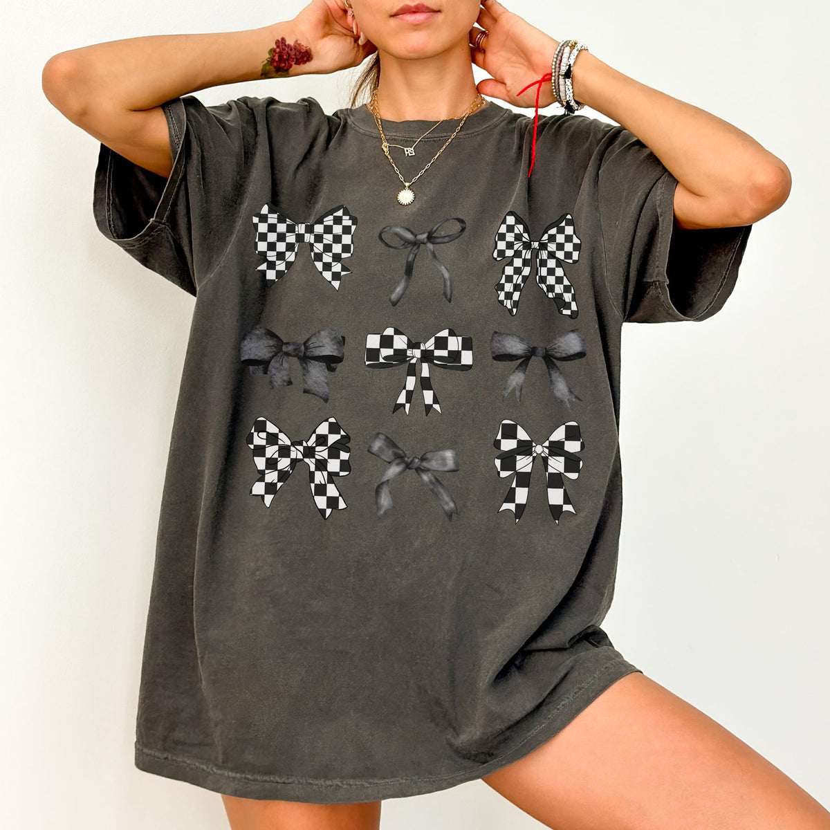 Model wearing an oversized pepper comfort color T-shirt featuring a grid of black, gray, and checkered bow graphics on the front.