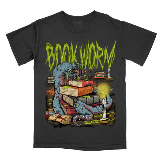 Black graphic T-shirt shown from the front featuring a blue worm wrapped around stacked books and candles, with the phrase “BOOK WORM” in green text across the top.