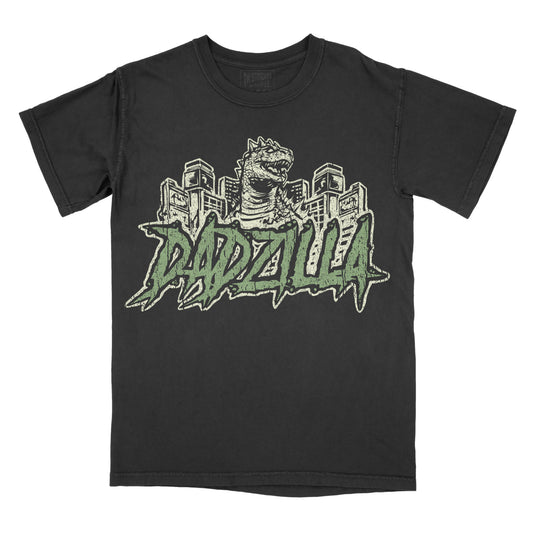 Black vintage-wash graphic T-shirt featuring a retro Godzilla-inspired monster towering over a city skyline above bold green graffiti-style lettering that reads "DADZILLA."