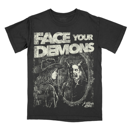 A black short-sleeve graphic t-shirt featuring the distressed white text 'FACE YOUR DEMONS' above a dark illustration of a horned figure in an oval mirror reflection, shown on a plain white background.