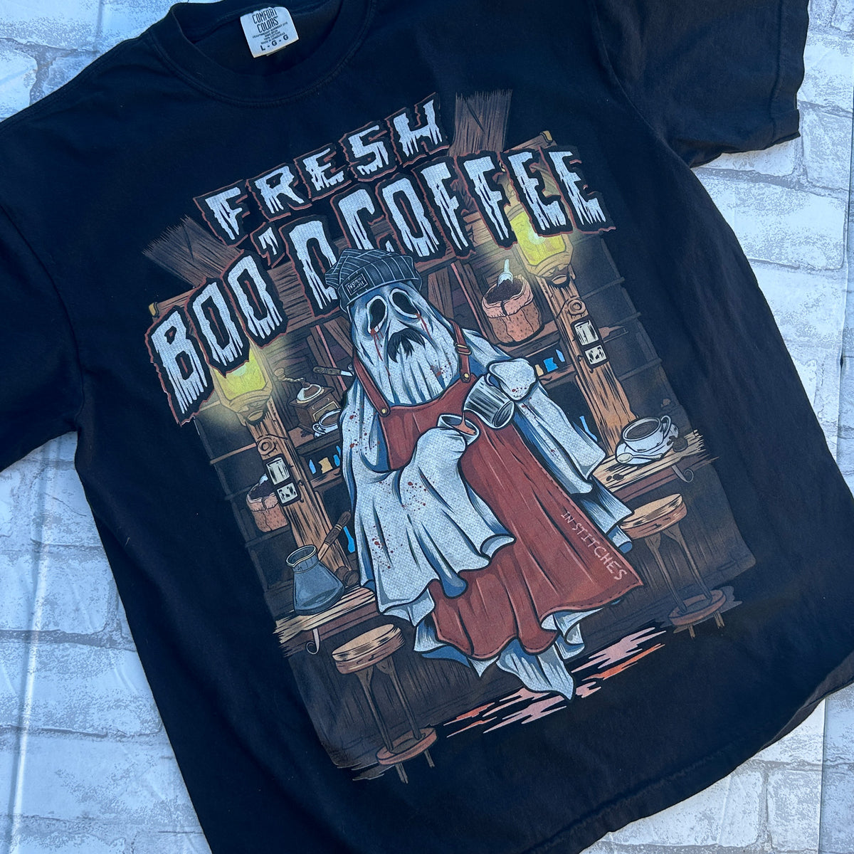 Black graphic T-shirt shown from the front, featuring a ghost barista illustration holding a coffee mug with the phrase “Fresh Boo'd Coffee” across the chest.