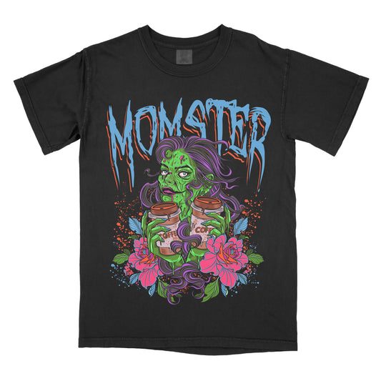 A graphic tee with a large print of a green monster character, surrounded by pink and blue floral designs, with the word 'MOMSTER' above it in bold lettering.