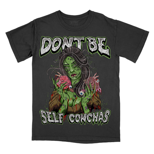 Front view of a black graphic T-shirt featuring green illustrated artwork and text reading “Don’t Be Self Conchas.”