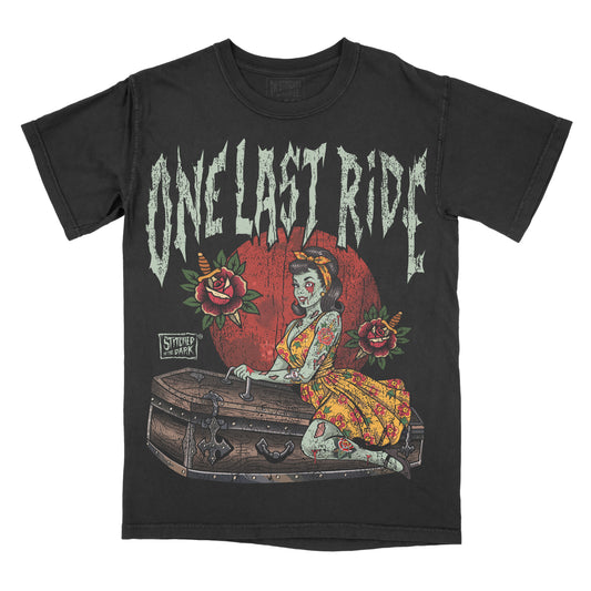 black T-shirt featuring a tattoo-style zombie pin-up woman sitting on a coffin, surrounded by roses and knives, with distressed text reading “One Last Ride” and Stitched in the Dark branding.