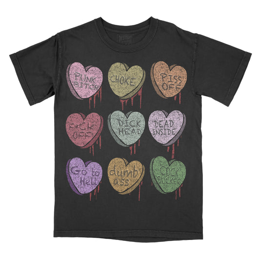 Black T-shirt featuring nine pastel conversation candy hearts arranged in a 3×3 grid. Each heart has a distressed vintage look with red dripping accents and contains a different phrase: "Punk Bitch," "Choke," "Piss Off," "Fuck Off," "I'd CK Instead," "Dead Inside," "Go to Hell," "Dumb Ass," and "Cock Sucker."